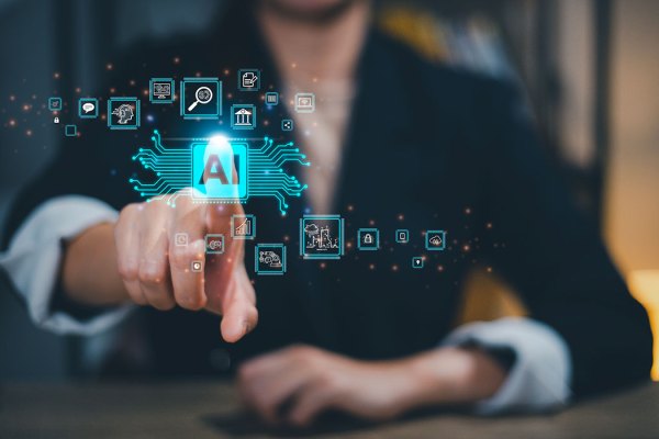 The image depicts a person in business attire reaching out towards a holographic display of various icons and symbols related to artificial intelligence (AI). Central to the display is an AI symbol, surrounded by other digital icons representing data analytics, technology, and automation processes, all connected by circuit-like lines, suggesting the integration of AI with various aspects of business and technology.